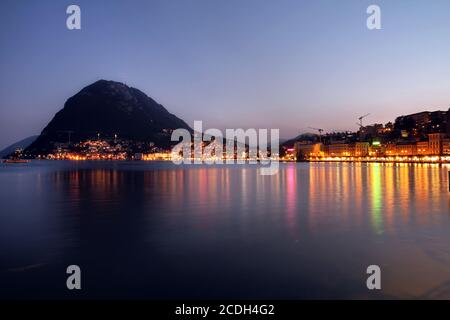 Sonnenuntergang über der Stadt Lugano in der Südschweiz (Kanton Tessin), mit Monte San Salvatore vom Seeufer. Stockfoto