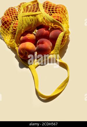 Nahaufnahme reife Pfirsiche in einem Netzbeutel oder String-Beutel auf hellgelben Hintergrund. Flach liegend. Keine Verschwendung. Stockfoto