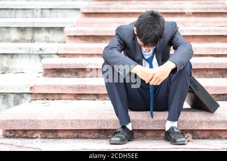 Ausfall arbeitslos betonte junge asiatische Geschäftsmann in Anzug. Ein junger Geschäftsmann sitzt verzweifelt auf der Treppe, weil niedrige Wirtschaftskrise. Entlassung. Stockfoto