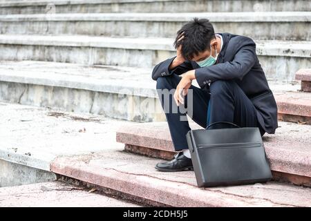 Ausfall arbeitslos betonte junge asiatische Geschäftsmann in Anzug, der Kopf mit Händen bedeckt. Ein junger Geschäftsmann sitzt verzweifelt auf der Treppe, weil niedrig Stockfoto