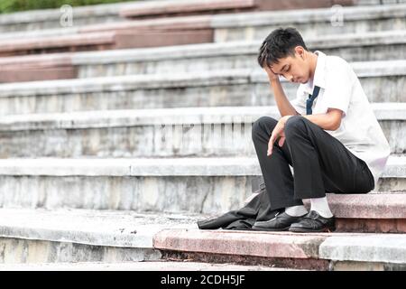 Ausfall arbeitslos gestresst junge asiatische Business-Mann über Kopf mit Händen. Ein junger Geschäftsmann sitzt verzweifelt auf der Treppe, weil niedrige economii Stockfoto