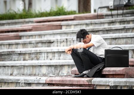Ausfall arbeitslos betonte junge asiatische Geschäftsmann. Ein junger Geschäftsmann sitzt verzweifelt auf der Treppe, weil niedrige Wirtschaftskrise. Entlassung. Stockfoto