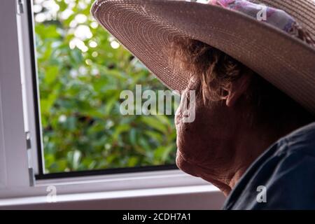 Ältere Frau mit Blick aus dem offenen Fenster des Landhauses Stockfoto