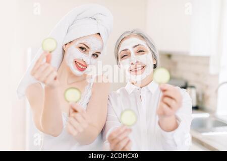 Morgens Hautpflege Routine, Familie Spa-Tag. Ziemlich ältere grauhaarige Frau und ihre junge attraktive Enkelin machen Ton Gesichtsmasken und posieren Stockfoto