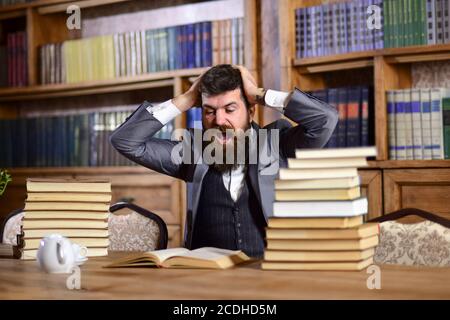 Mann im klassischen Anzug oder Professor mit verrückten Gesicht sitzt in der Bibliothek, Bücherregale auf dem Hintergrund, entkokelt. Forscher suchen in Buch, halten Sie den Kopf wie etwas schockierendes finden. Wissenschaft und Studium Konzept Stockfoto