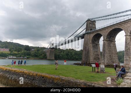 Touristen versammeln sich am Fuße der Hängebrücke von Thomas Telford an der Menai Bridge auf der Isle of Anglesey, Wales, Großbritannien. Stockfoto