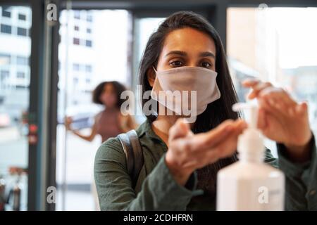 Geschäftsfrau, die Handgel verwendet, bevor sie das Büro an der Rezeption betritt Stockfoto