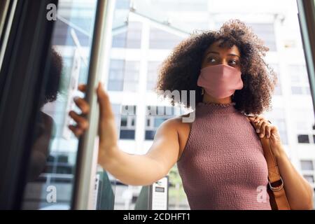 Junge Erwachsene Frau, die ins Büro kommt, trägt Gesichtsmaske und schaut weg Kamera Stockfoto