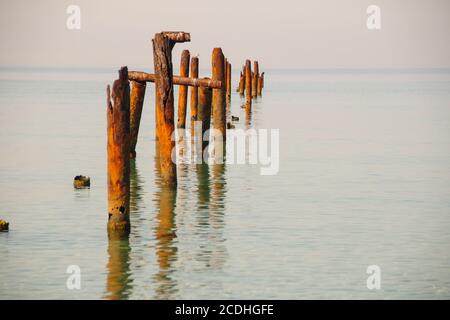 Seascape mit blauem ruhigem Wasser und Reihen von rostigen Rohren mit grünen Algen am Sommertag. Rostpfeifen, die vom alten Pier übrig geblieben sind. Perspektive, die zu führt Stockfoto