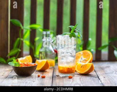 Sanddorneis Limonade mit Orangen. Früchte und Beeren im Freien auf einem Holztisch. Entgiftungsgetränke. Selektiver Fokus, Kopierbereich Stockfoto