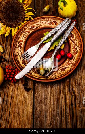 Abendessen im Herbst und Thanksgiving. Ernte von Kürbissen und Beeren, bunte Blätter, Keramikplatten, Gabel, Löffel und Messer. Fallbesteck w Stockfoto