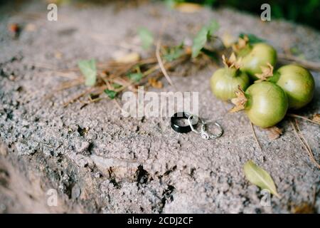 Verlobungsring der Braut und Ringe der Braut und des Bräutigams auf Steinstruktur mit kleinen Granatapfelfrüchten. Stockfoto
