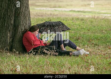 WIMBLEDON LONDON, GROSSBRITANNIEN - 28. AUGUST 2020 . Junge Frauen schützen sich am Wimbledon Common neben einem Baum vor den Regenschauern. Kredit: amer ghazzal/Alamy Live Nachrichten Stockfoto