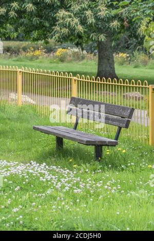 Überwucherter, einsamer öffentlicher Sitz/Bank auf einem Kinderspielplatz, der während der britischen Covid-Sperre von Menschen leer war. Verlassene öffentliche Räume, leere Parkbank in Großbritannien. Stockfoto