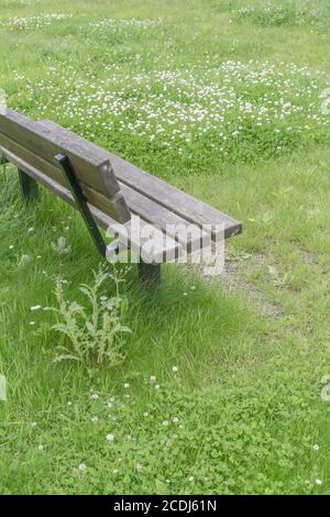 Überwucherter, einsamer öffentlicher Sitz/Bank auf einem Kinderspielplatz, der während der britischen Covid-Sperre von Menschen leer war. Verlassene öffentliche Räume, leere Parkbank in Großbritannien. Stockfoto