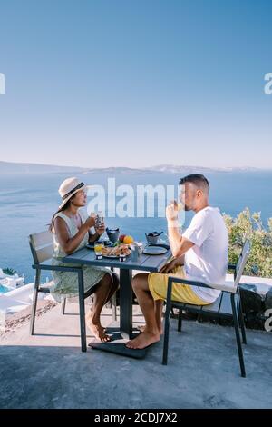 Pärchen beim Frühstück im traditionellen Höhlenhaus Santorini Griechenland, wunderschönes weiß getünchtes Dorf Oia mit Kirche und Windmühle während des Sonnenuntergangs Stockfoto