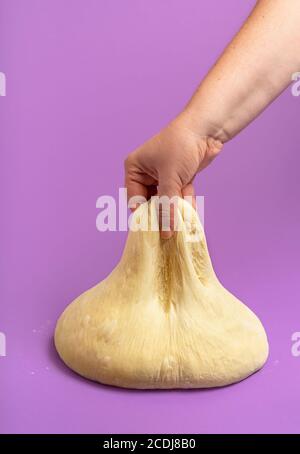 Brotteig isoliert auf einem nahtlosen violetten Hintergrund. Frau Hand Stretching der gesäuerten Teig. Handgefertigter Donut-Teig. Ungekochte Pizzateig. Stockfoto