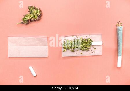 Schritte und Materialien, um ein Marihuana-Gelenk auf rosa Hintergrund Rollen. Stockfoto