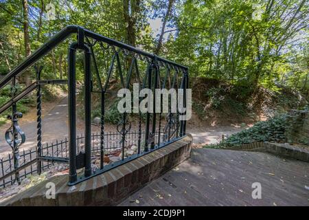 Schwarzes schmiedeeisernes Geländer auf einer Treppe, die zu einer Kapelle mit einer Landstraße und üppig grünen Bäumen führt, sonniger Sommertag in Süd-Limburg, Niederlande Stockfoto