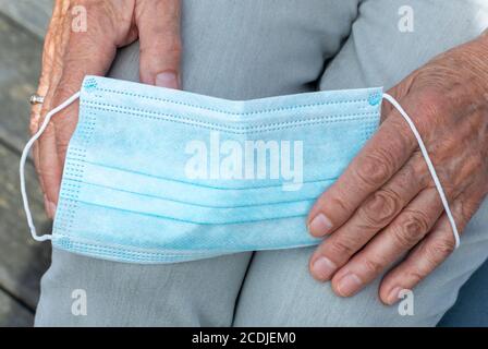 Hände einer älteren Frau, die eine medizinische Schutzmaske in der Hand hält, Nahaufnahme. Stockfoto