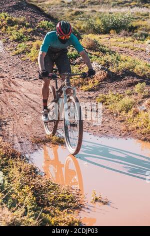 Mountain Biker trägt eine Schutztuch Gesichtsmaske Reiten durch Eine schlammige Pfütze Stockfoto