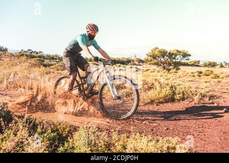 Mountain Biker trägt eine Schutztuch Gesichtsmaske Reiten durch Eine schlammige Pfütze Stockfoto