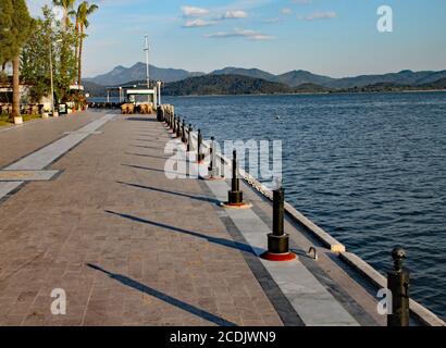 Die Abendsonne sinkt langsam im Westen und wirft Schatten vom Geländer auf einen dekorativen Gehweg in einem türkischen Badeort. Stockfoto