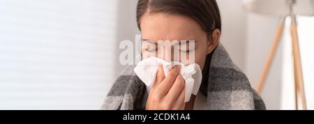 Kranke Frau fühlt sich unwohl zu Hause zu bleiben. Junges Mädchen mit Grippe-Symptome Husten in Gewebe über Nase beim Niesen als COVID 19 Prävention. Panorama Stockfoto