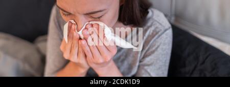 Kranke Frau fühlt sich zu Hause unwohl. Junges Mädchen mit Grippe-Symptome Husten in Gewebe über Nase beim Niesen als COVID 19 Prävention. Panoramakultur Stockfoto