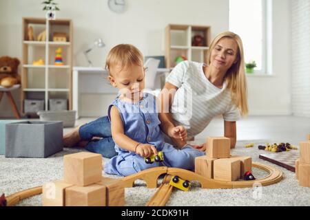 Junge Babysitter und kleines Kind spielen mit Holzklötzen in Gemütlicher Kinderzimmer Stockfoto