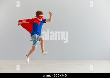 Kleiner Junge in einem Superhelden-Kostüm sprang auf einen grauen Hintergrund. Superhelden-Kind. Kinderkostüm. Stockfoto