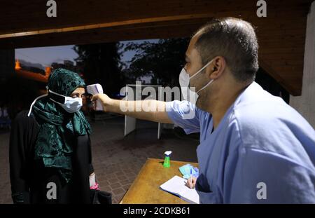 Khan Younis, Stadt im Gazastreifen von Khan Younis. August 2020. Am 28. August 2020 misst ein palästinensischer Gesundheitshelfer die Körpertemperatur einer Frau im Al Amal Krankenhaus in der Stadt Khan Younis im südlichen Gazastreifen. In Palästina gab es in den letzten 24 Stunden zwei Todesfälle und 724 neue COVID-19 Fälle in den palästinensischen Gebieten, teilte ein hochrangiger palästinensischer Beamter am Freitag mit. Kredit: Yasser Qudih/Xinhua/Alamy Live Nachrichten Stockfoto