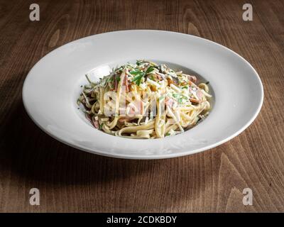 Carbonara, traditionelle italienische Küche, serviert auf weißem Teller auf einer Holzoberfläche Stockfoto
