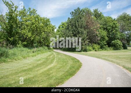 Fahrrad- und Fußgängerweg durch üppige Frühlingsflora entlang des Waubonsie Creek Trail in Aurora, Illinois Stockfoto