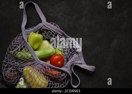 Graue Sack String Beutel mit Gemüse, Zucchini, Paprika, Karotten, Rüben, Zwiebeln schwarzen Hintergrund. Ernte aus Garten frisches helles Gemüse.Konzept ze Stockfoto