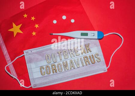 DAS AUSBRUCH-CORONAVIRUS ist eine Formulierung auf einer schützenden medizinischen Maske. Chinas Flagge, Tablets und elektronisches Thermometer auf rotem Hintergrund. Coronavirus 2019 d Stockfoto