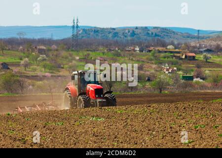 Der Bauer das Feld pflügen. Traktor im Bereich Pflege. Roter Traktor mit einem Pflug in einem Bauernhof-Feld. Traktor und Pflug Stockfoto