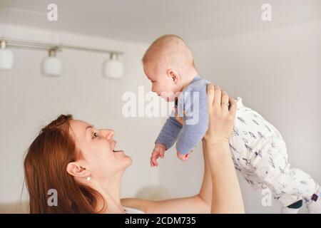 Mutter spielt mit seinem kleinen Sohn, hält ihn in den Händen über ihrem Kopf, sieht aus wie Fliege Stockfoto