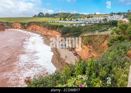 Wellen brechen an den Strand von Ladram Bay in der Nähe von Exmouth in South Devon, England, Großbritannien. Rote Sandsteinklippen, Teil der Jurassic Coast. Stockfoto