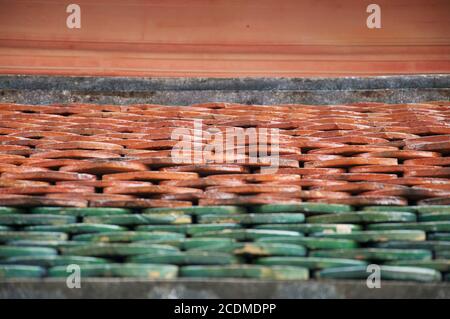 Flache perspektivische Ansicht von grünen und roten Terrakotta-Dachziegeln auf einem buddhistischen Tempel in Asien. Stockfoto