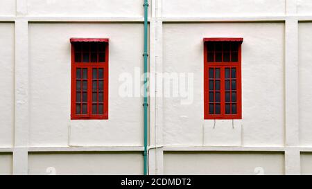 Nahaufnahme von zwei roten Fenstern in einem restaurierten alten Kolonialgebäude mit weißen Steinmauern. Stockfoto