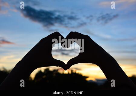 Silhouette Hand in Herzform mit Sonnenuntergang, Valentinstag Konzept. Stockfoto