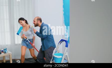 Junges Paar, das Spaß hat, während sie ihre Wohnung renovieren. Konstruktion, Dekoration, Pinsel. Wohndekoration und Renovierung in gemütlichen Wohnung Wohnung, Reparatur und Verjüngungskur Stockfoto