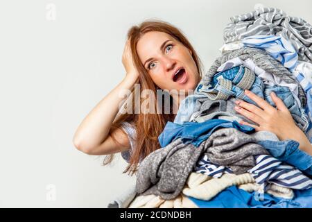 Schockierte kaukasische Hausfrau hält Haufen schmutziger Kleidung. Stockfoto