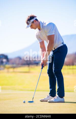 Mitte der zwanziger Jahre männlichen Golfer Planung seiner Putting Schuss auf die PIN auf einem Grün an einem hellen sonnigen Tag Stockfoto