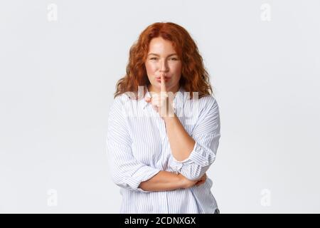 Wunderschöne mittleren Alters Rotschopf Frau fragen ruhig zu halten, Erwachsene Frau sagen, schweigen, shushing mit Finger auf die Lippen gedrückt. Mutter erzählt das Geheimnis, huschend Stockfoto