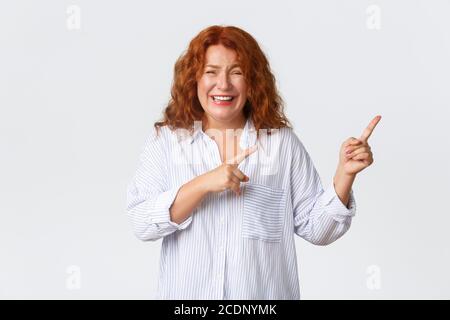 Glücklich wunderschöne Rothaarige Frau, Dame mittleren Alters lachen über etwas lustig, kichern und zeigen Finger oben rechts Ecke, Banner zeigen Stockfoto
