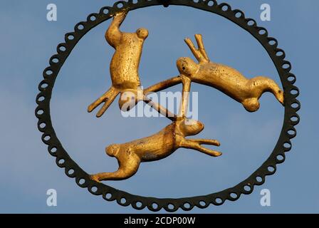 Drei goldene Hasen, verbunden durch ihre langen Ohren, springen um das Metallzeichen ‘Drei Hasen’, einem historischen Hotel-Restaurant in Braunstraße, Michelstadt, Odenwald, Hessen. Das Symbol wurde verschiedentlich als ein altes Versprechen guter Gastfreundschaft, ein Webergilde-Emblem (mit den Ohren, die ein Shuttle darstellen) interpretiert - und sogar als Hinweis auf das mittelalterliche System der Dreifeld-Landwirtschaft. Stockfoto