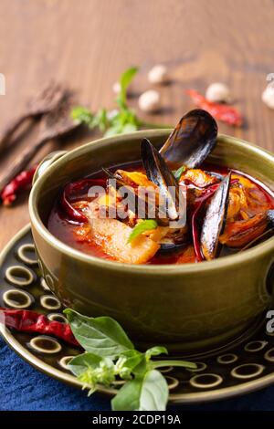 Speisekonzept Thai sauer rot Curry Muscheln Ananas Kang Kua Hoi in grüner Keramikschale auf blauem Serviettenholz Hintergrund Mit Kopierbereich Stockfoto