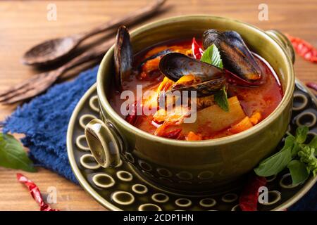 Speisekonzept Thai sauer rot Curry Muscheln Ananas Kang Kua Hoi in grüner Keramikschale auf blauem Serviettenholz Hintergrund Mit Kopierbereich Stockfoto